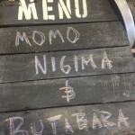 Chalk writing on the rustic menu board at Alchemy chef Ricardo Heredia's food stand lists the two types of Japanese skewers he was grilling at the Street Food Market party held in the San Diego Public Market on March 24, 2013. Momo nigma is a mix of chicken and Japanese scallions. Butabara is pork belly. (Photo by Cyndia Zwahlen for the Small Biz Mix.)