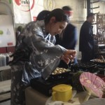 Dressed in a grey kimono, Stephanie Obayashi, kitchen chef at Azuki Sushi Lounge of San Diego, uses two skewers to turn takoyaki or octopus puffs, a popular Japanese Street food, in a special multi-mold pan. The stand was one of dozens at the Street Food Market party held March 24, 2013 in the San Diego Public Market. (Photo by Cyndia Zwahlen for the Small Biz Mix.)