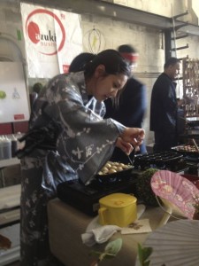 Dressed in a grey kimono, Stephanie Obayashi, kitchen chef at Azuki Sushi Lounge of San Diego, uses two skewers to turn takoyaki or octopus puffs, a popular Japanese Street food, in a special multi-mold pan. The stand was one of dozens at the Street Food Market party held March 24, 2013 in the San Diego Public Market. (Photo by Cyndia Zwahlen for the Small Biz Mix.)