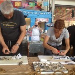 Erik Gosswiller, left, and Maylin Chavez open local oysters at chef Melissa Mayer's Pacific Standard Oyster Co. food cart at the Street Food Market party held March 24, 2013 in the San Diego Public Market. Mayer, who runs Martini Media, is event co-chair.(Photo by Cyndia Zwahlen for the Small Biz Mix.)