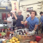 Fruit juices, herbs and veggies mix with galvanized steel tubs packed with ice, liquor, wines and local beer at the cocktail station run by the Queen-Connor-Ward Collective for the Street Food Market party at the San Diego Public Market, March 24, 2013. Jen Queen caps a cocktail shaker at left. Ian Ward, center, works another cocktail shaker while Justin Hockemeyer, right, leans out to offer a citrus-garnished drink. (Photo by Cyndia Zwahlen for the Small Biz Mix)