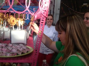 A woman plucks a strawberry-rhubarb pie pop out of its bed of sugar in a glass box on a fanciful pink-metal dessert cart at the Street Food Market party in the San Diego Public Market, March 24, 2013. (Photo by Cyndia Zwahlen for Small Biz Mix)