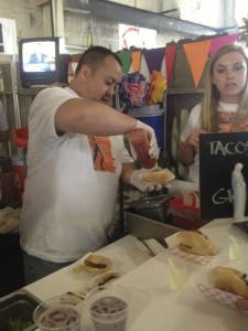 Keoni Simmons, left, prepares a hot dog wrapped in bacon, Tijuana-style, with Kristin Lieb at the Andrew Spurging(TM) TJ Dogs stand at the Street Food Market Party held March 24, 2013 in the San Diego Public Market. Spurgin, my brother-in-law, was the event co-chair. (Photo by Cyndia Zwahlen for the Small Biz Mix.)