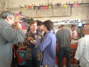 A group of partygoers eat Tijuana-style hot dogs, or TJ dogs, at the Street Food Market party March 24, 3013 in the San Diego Public Market. The banner in Spanish in the backgrounds reads, "Put your hands up and open your mouth!" (Photo by Cyndia Zwahlen for the Small Biz Mix.)