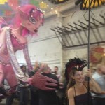 Smiling puppeteer Bridget Rountree of Animal Crackers Conspiracy Puppet Co. in San Diego, holds aloft a large butterfly on a stick while leading the giant pink-haired fairy puppet who is hugging a partygoer behind her at the Street Food Market fest held March 24, 2013 in the San Diego Public Market. (Photo by Cyndia Zwahlen for the Small Biz Mix.)