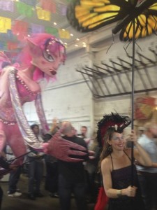 Smiling puppeteer Bridget Rountree of Animal Crackers Conspiracy Puppet Co. in San Diego, holds aloft a large butterfly on a stick while leading the giant pink-haired fairy puppet who is hugging a partygoer behind her at the Street Food Market fest held March 24, 2013 in the San Diego Public Market. (Photo by Cyndia Zwahlen for the Small Biz Mix.)
