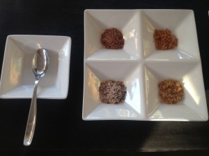 Samples of four rust-colored gourmet sea salts in a divided white dish with a tiny tasting spoon at the Salt Farm booth during the March 24, 2013 Street Food Market party at San Diego's Public Market. (Photo by Cyndia Zwahlen for the Small Biz Mix.)